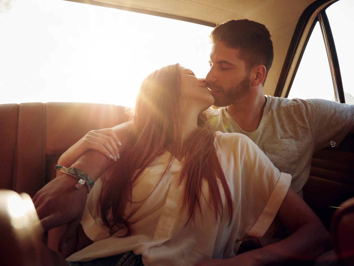 Frau und Mann im Auto, die sich verliebt anschauen und küssen.