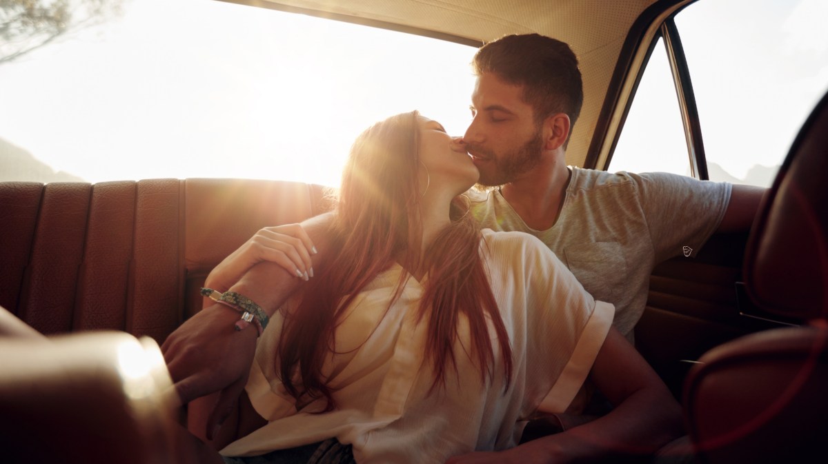 Frau und Mann im Auto, die sich verliebt anschauen und küssen.