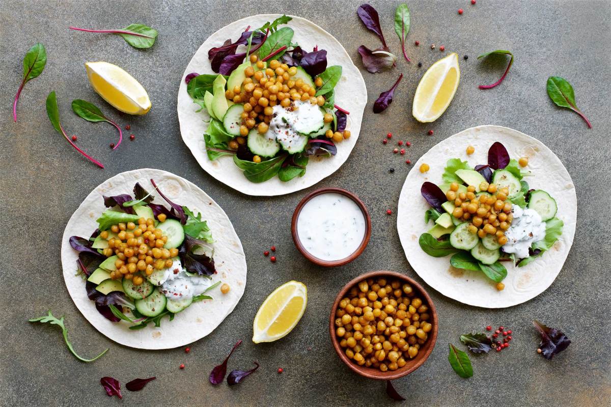 Veganer Tortilla-Kichererbsen-Avocado-Salat mit Gurke und Joghurtsoße. Gesundes Clean Eating Food Konzept. Gesundes Essen, angerichtet auf weißen Tellern.