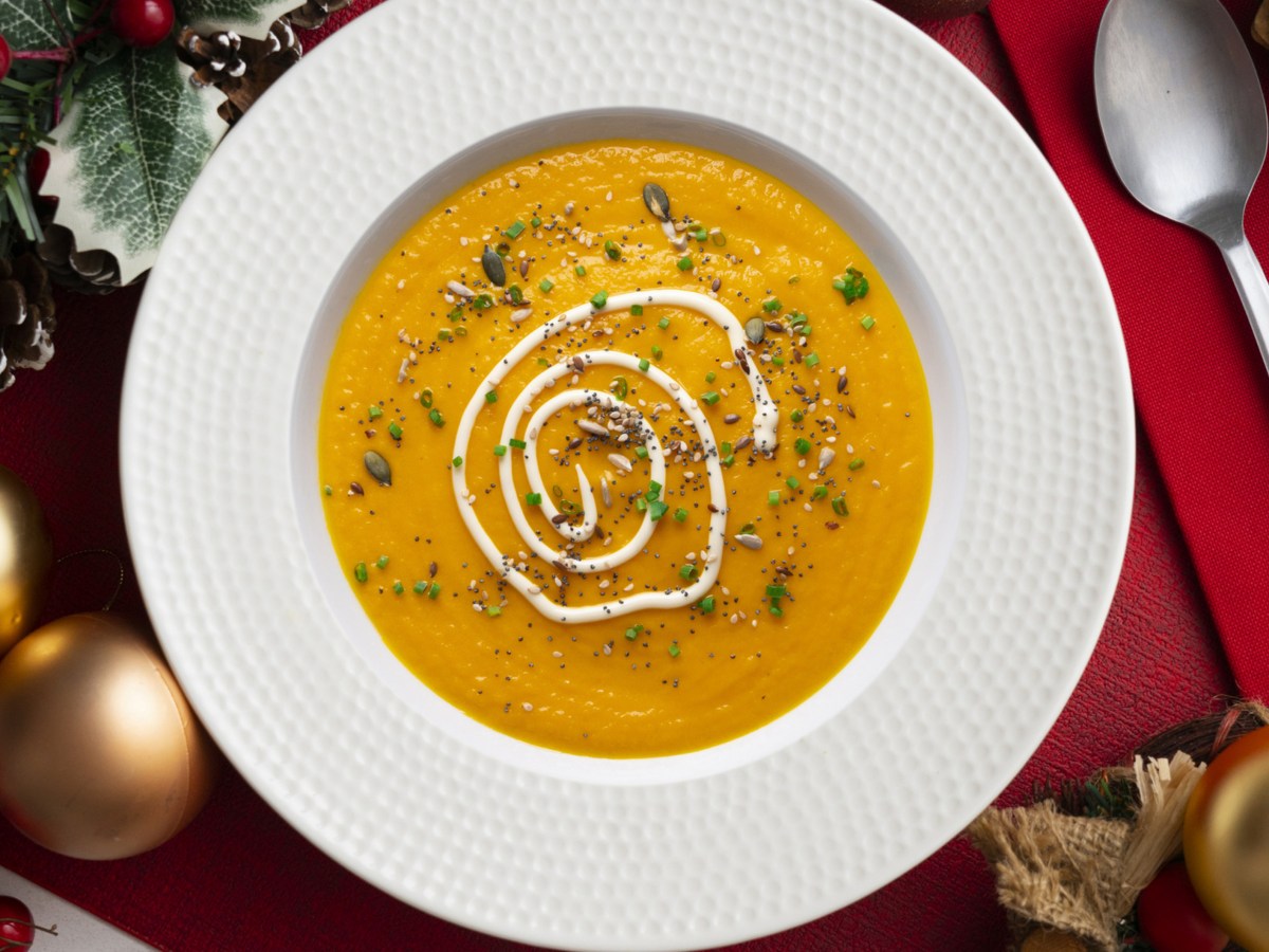 Cremige Karottensuppe in weißem Teller auf weihnachtlich gedeckten Tisch.