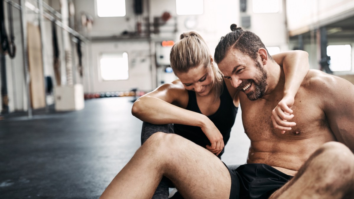 Ein Mann und eine Frau, die sich im Fitnessstudio in den Armen liegen und lachen