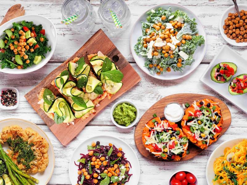 Gesunde pflanzenbasierte Low-Carb-Diät-Tischszene. Blick von oben auf einen weißen Holzhintergrund. Blumenkohl-Fladenbrot und Steak, Gemüsenudeln, Grünkohlsalate, gefüllte Avocados und Süßkartoffeln.