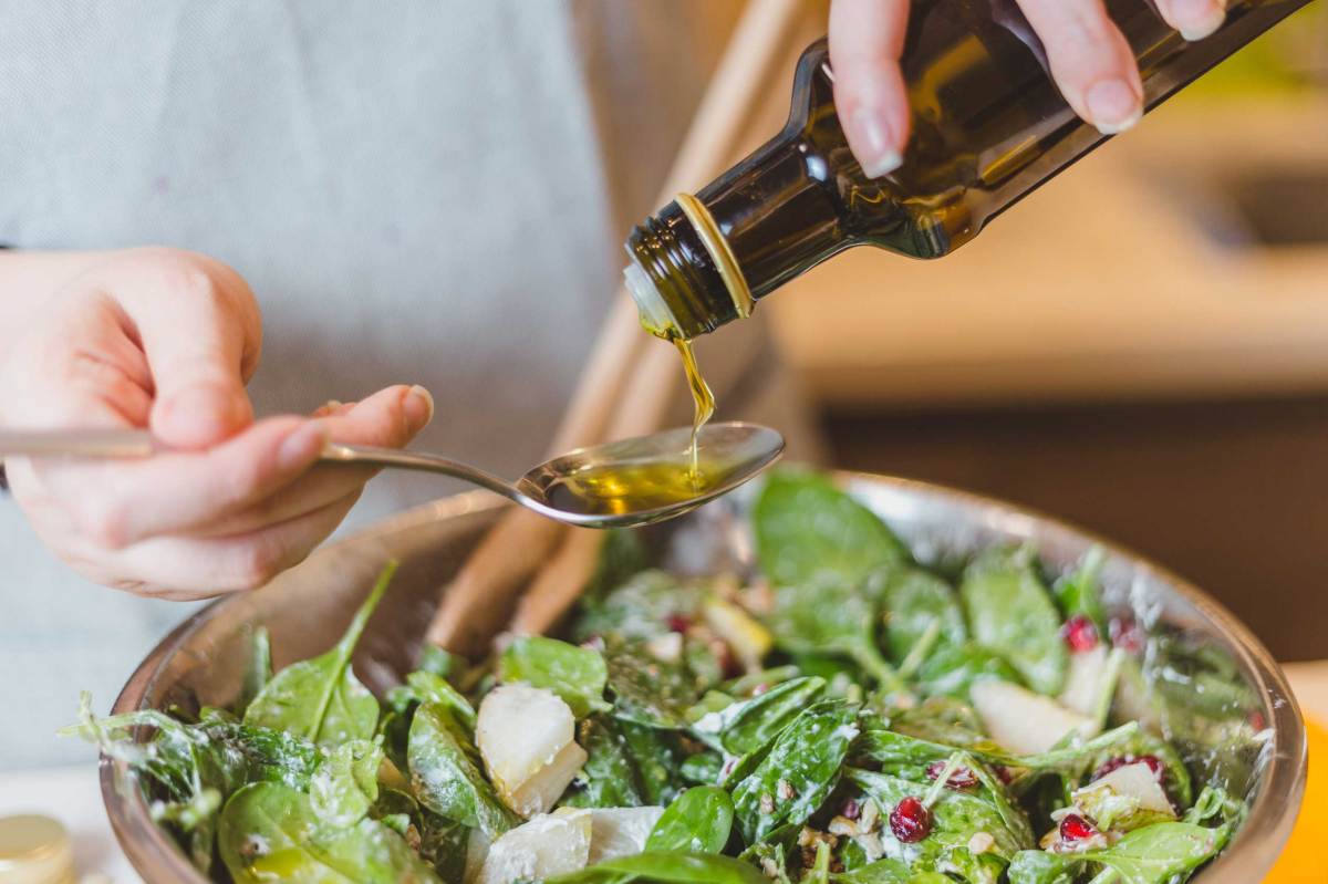 Nahaufnahme von Händen, die natives Olivenöl über Salat gießen