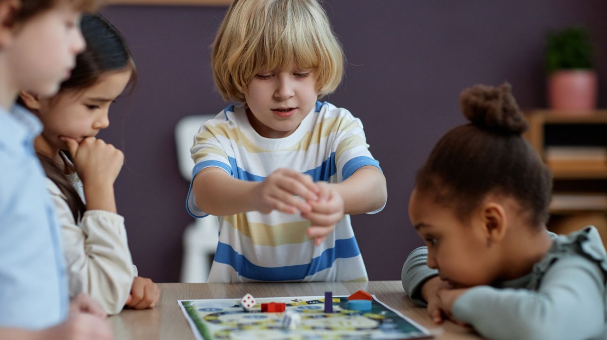 4 Kinder der ersten Klasse sitzen an einem Tisch und spielen ein Würfelspiel.