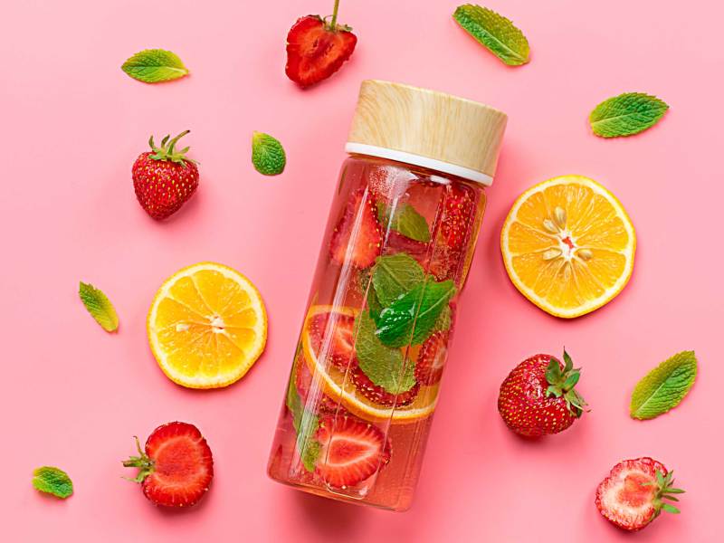 Erdbeere infundiert Wasser, Cocktail, Limonade oder Tee. Sommer eisgekühltes Kaltgetränk mit Erdbeere, Zitrone und Minze auf rosa Hintergrund. Flach gelegt. Ansicht von oben.