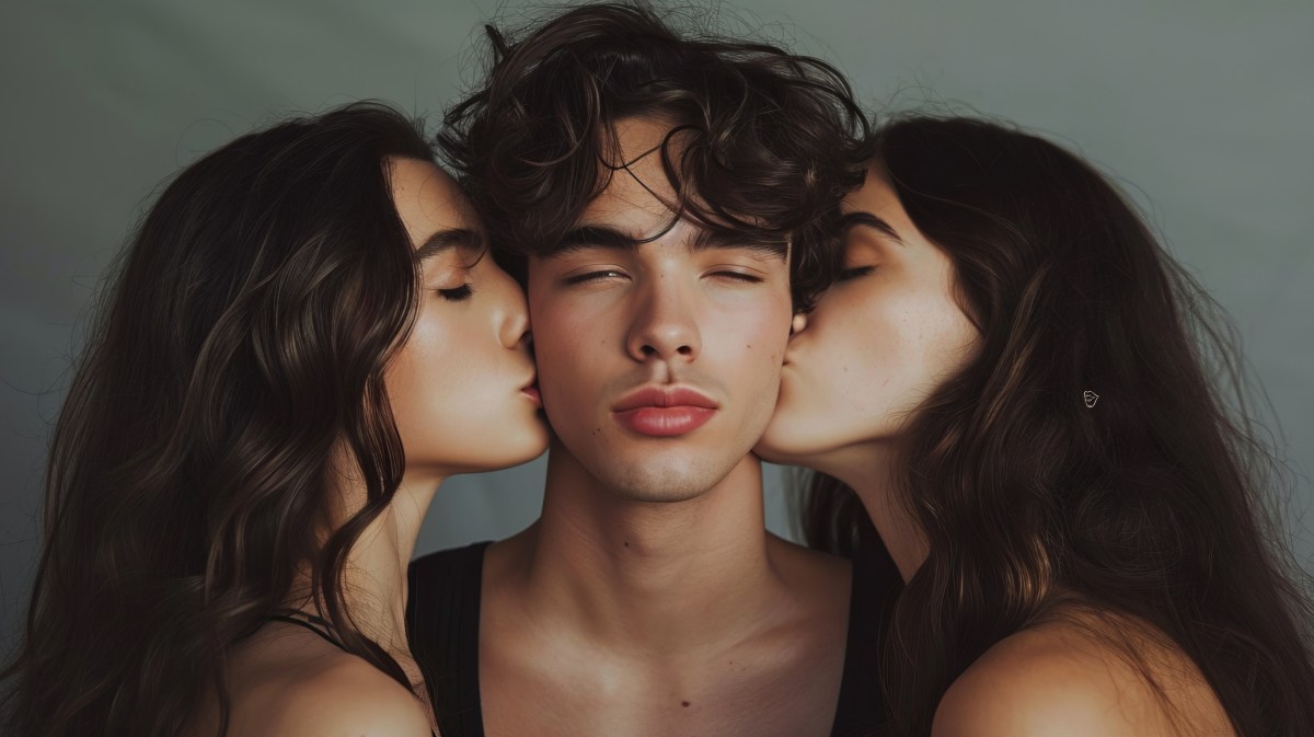 Zwei Frauen vor einer grauen Wand, die einen Mann in der Mitte auf die Wange küssen.