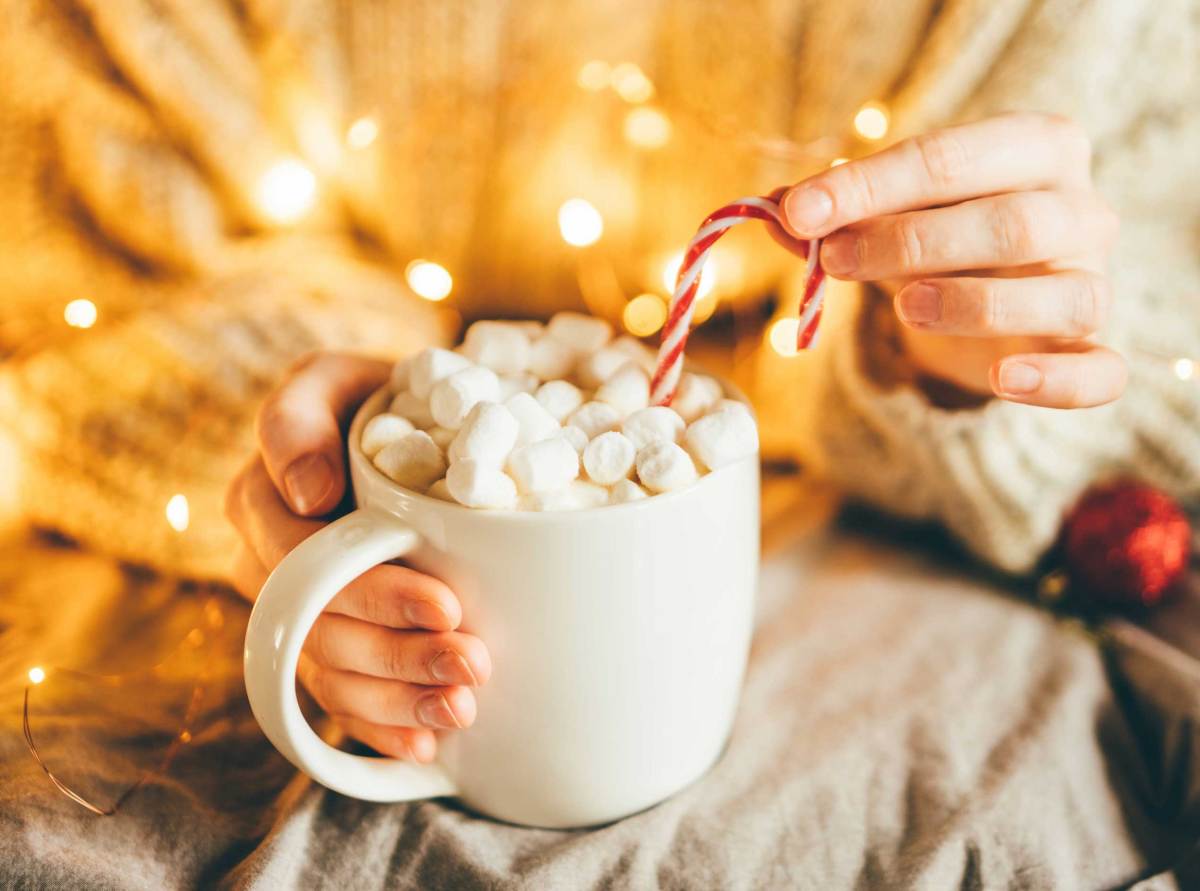 Frau hält Tasse mit heißer Schokolade, Marshmallows und Zuckerstange