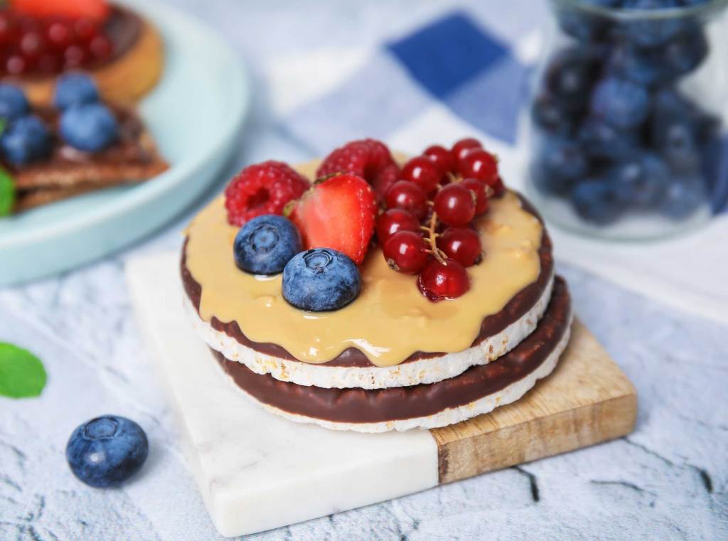 Reiswaffeln mit Schokolade, Beerenfrüchten und Erdnusscreme auf hellem Untergrund