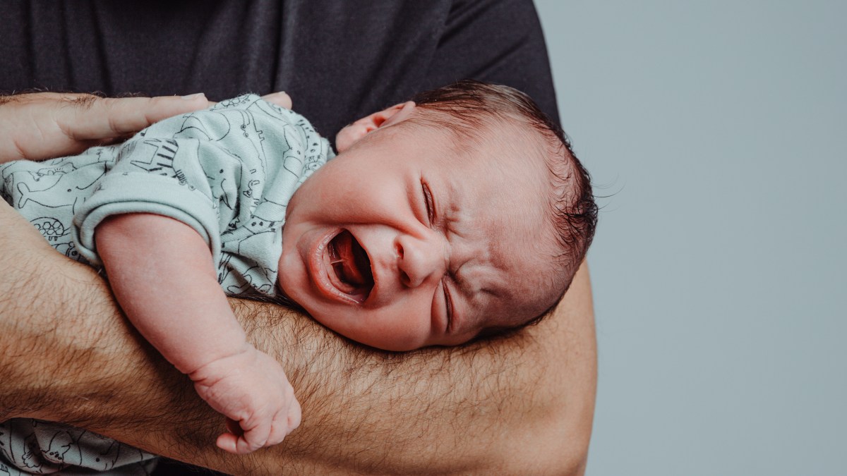 Weinendes Baby, dass auf dem Unterarm eines Mannes liegt.