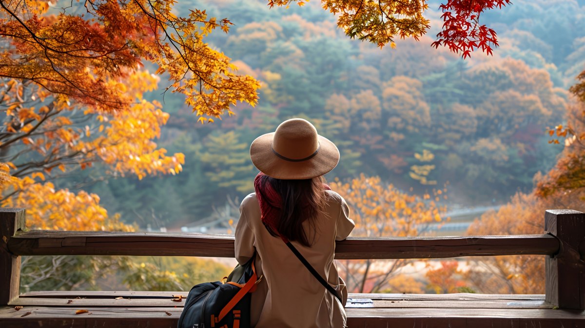 Frau mit Hut sitzt auf einer Bank unter herbstlichen Bäumen