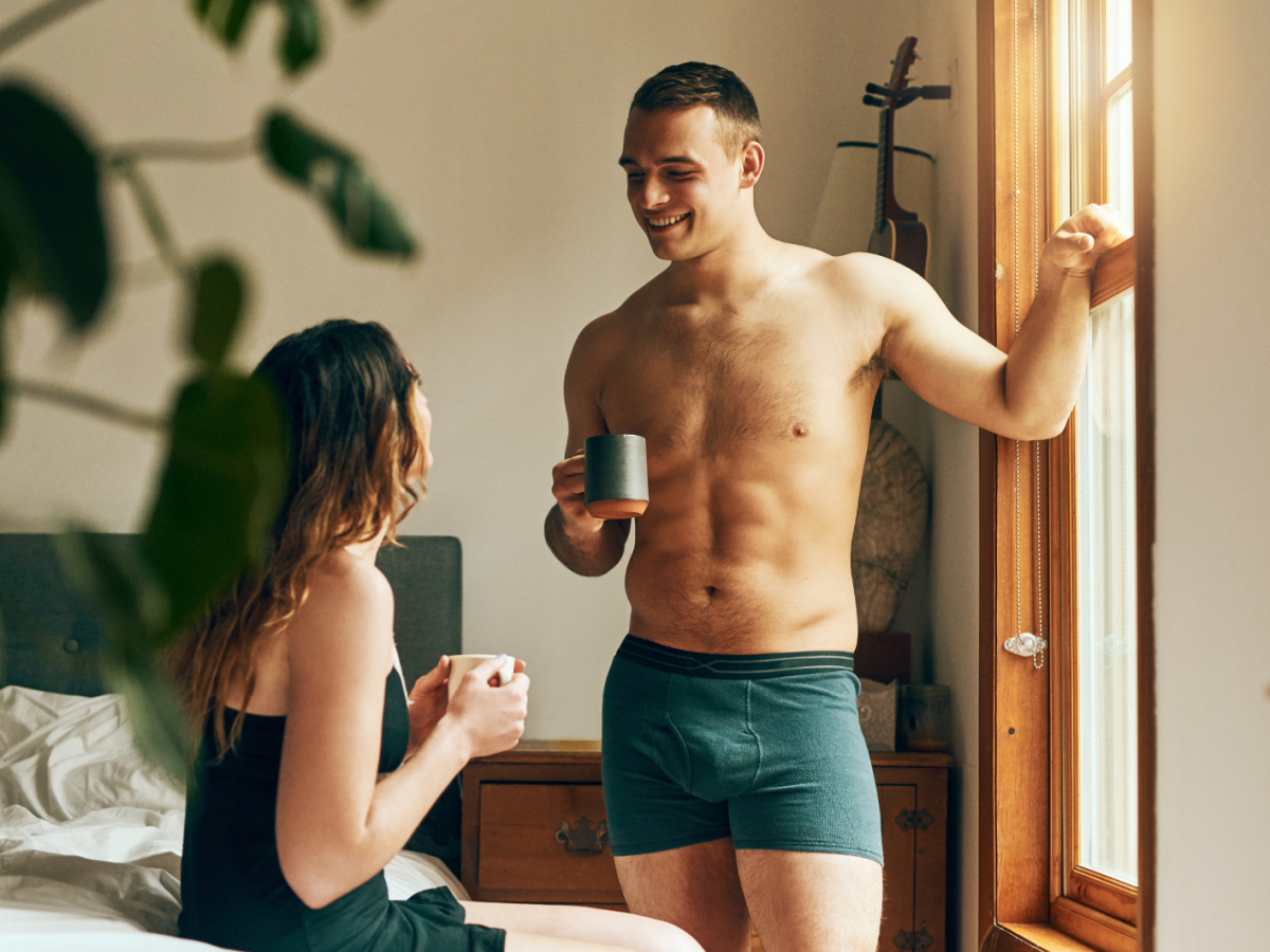 Mann und Frau im Schlafzimmer, die Kaffeetrinken, sich unterhalten und anlachen.