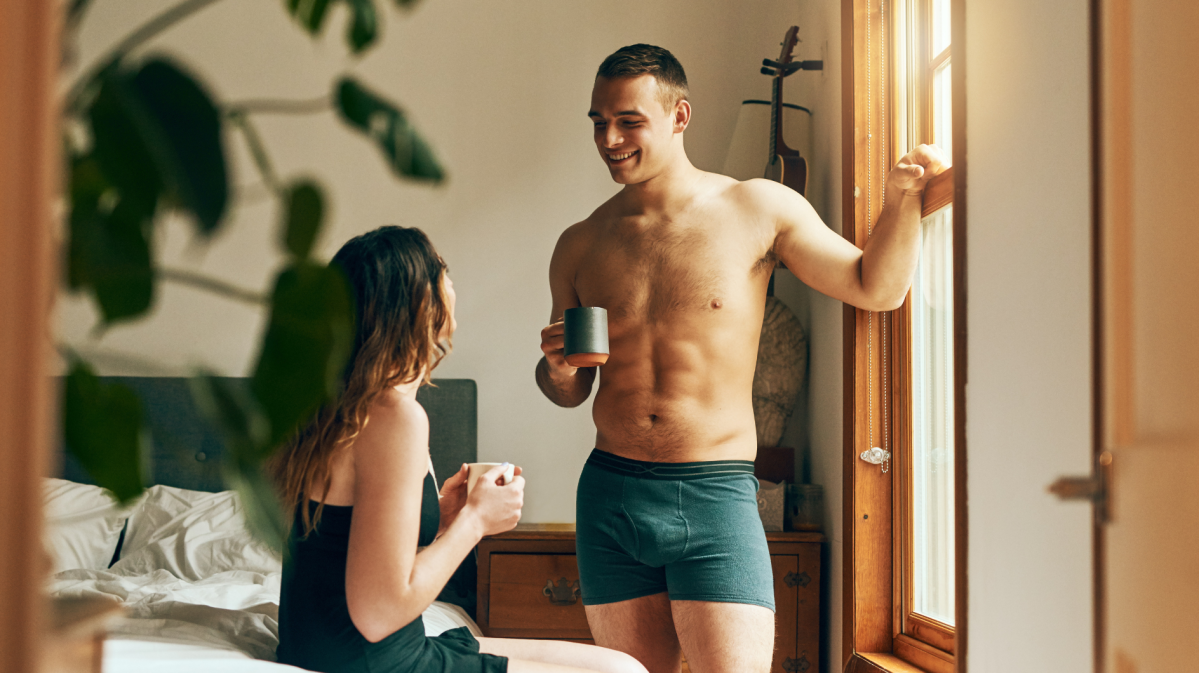 Mann und Frau im Schlafzimmer, die Kaffeetrinken, sich unterhalten und anlachen.