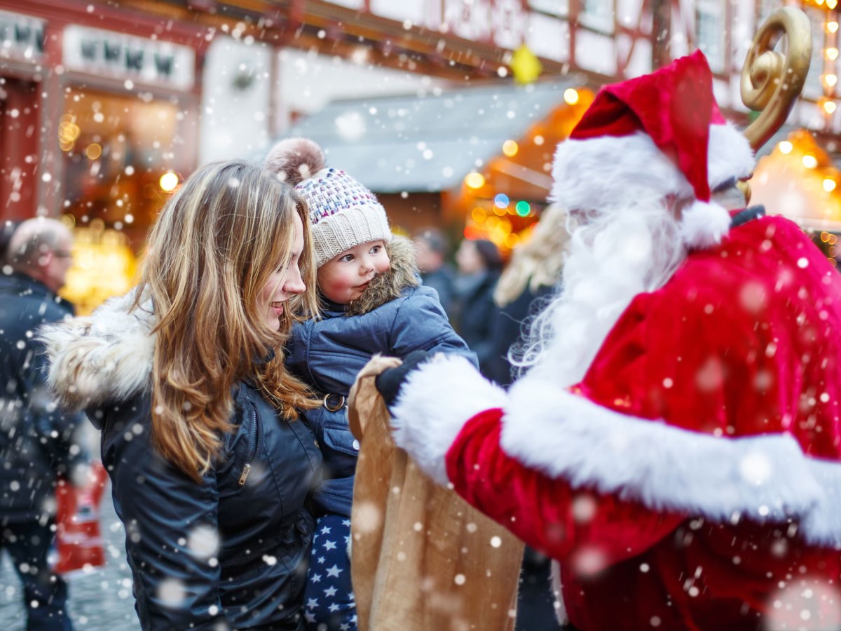 Kleines Kind sitzt auf dem Arm seiner Mutter und beide stehen dem Weihnachtsmann gegenüber.