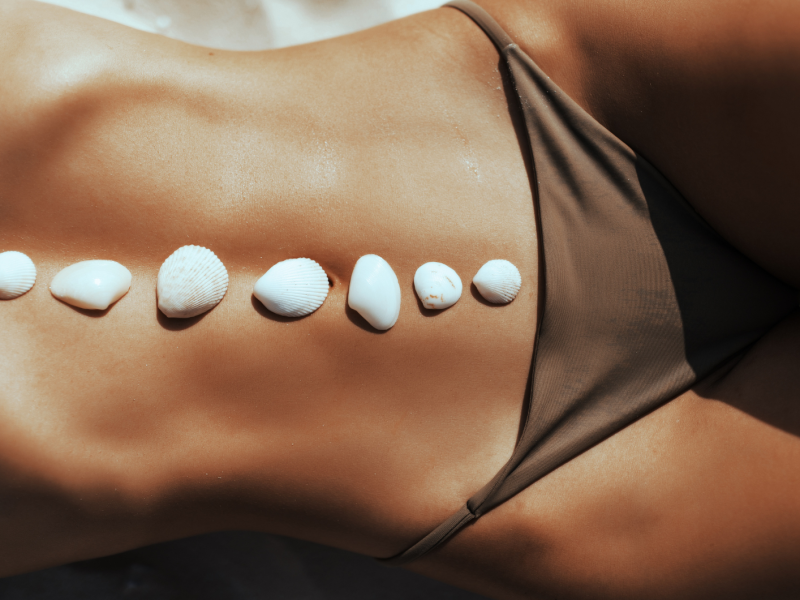 Frau am Strand im Bikini mit Muscheln auf dem Bauch.