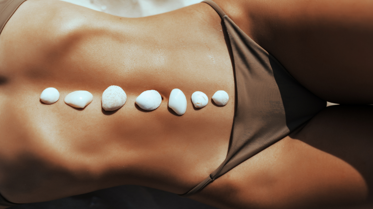 Frau am Strand im Bikini mit Muscheln auf dem Bauch.