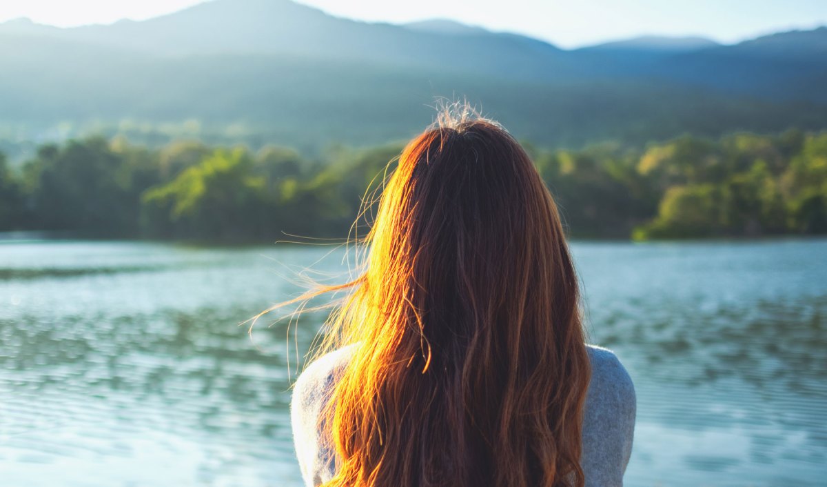 Eine junge Frau sitzt an einem See und schaut auf das Wasser