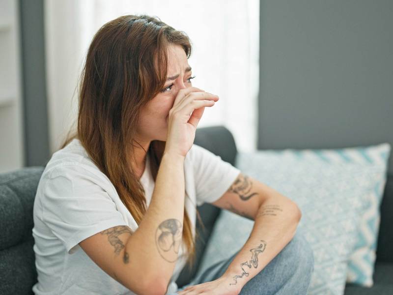 Frau sitzt weinend auf ihrem Sofa,