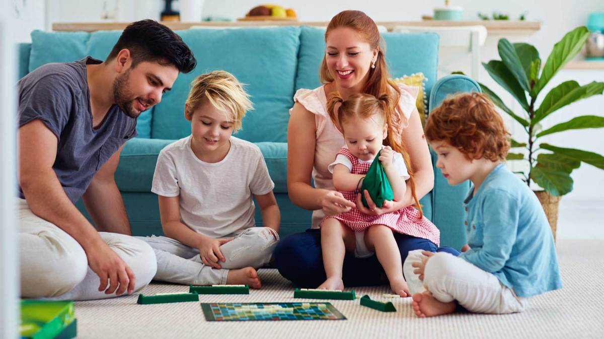 Mutter, Vater und die drei Kinder unterschiedlichen Alters spielen eine Runde Scrabble auf dem Fußboden.