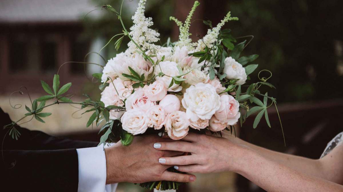 Frau und Mann halten gemeinsam einen Brautstrauß mit vielen Rosen.