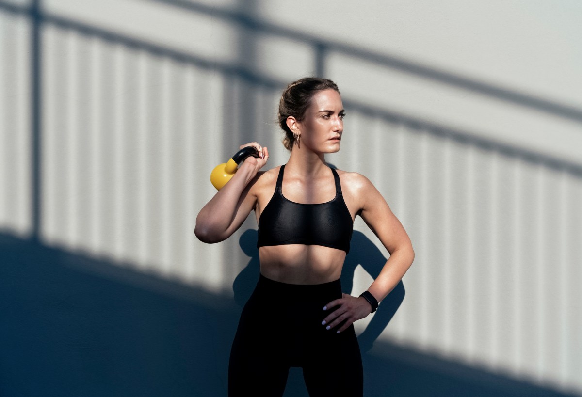 Krafttraining Frauen: Trainierte Frau in Sport-BH und Leggings mit gelber Kettlebell vor Wand