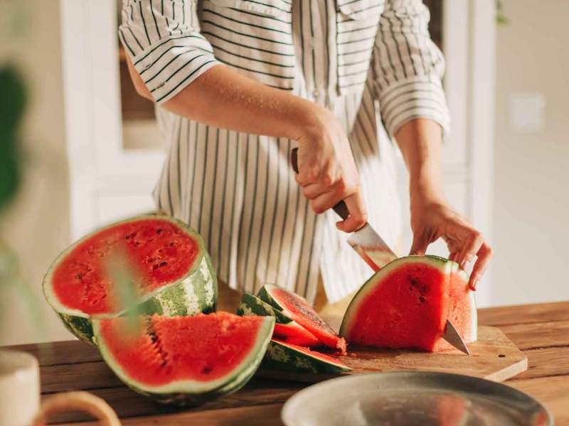 Frau schneidet mit einem großen Messer eine Wassermelone