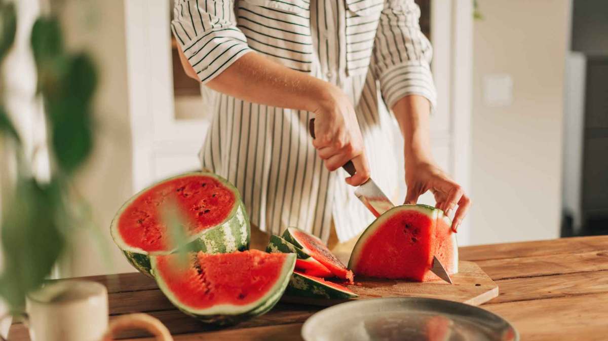 Frau schneidet mit einem großen Messer eine Wassermelone