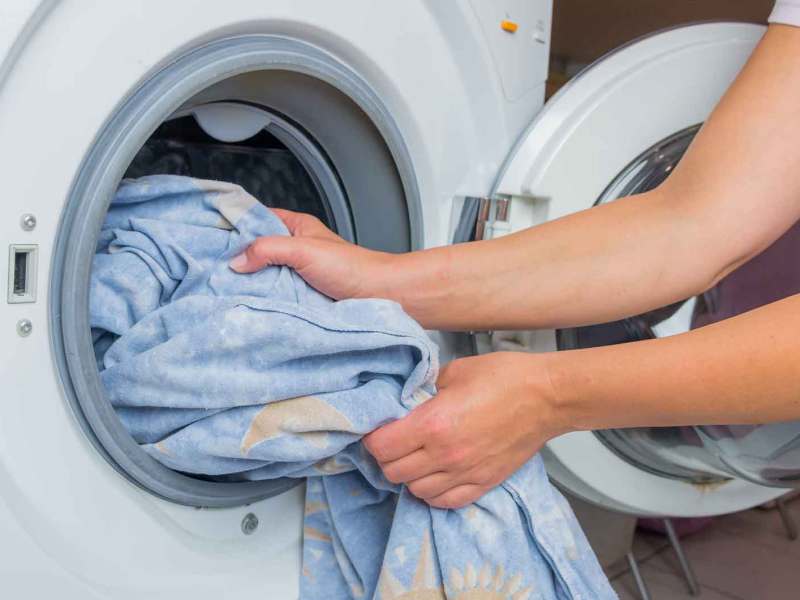 Frau wirft Wäsche in die Waschmaschine.