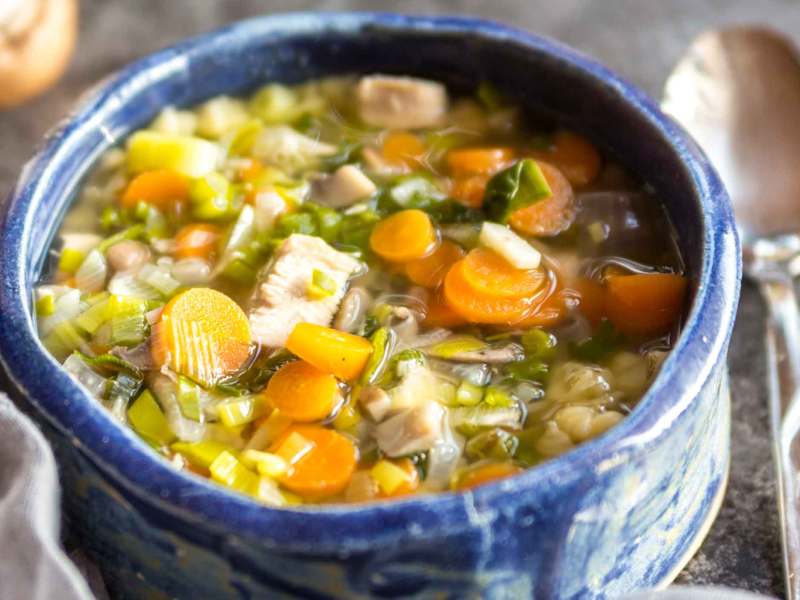 Blaue mediterrane Schüssel mit einer klaren Hühnersuppe mit Viel Gemüse.