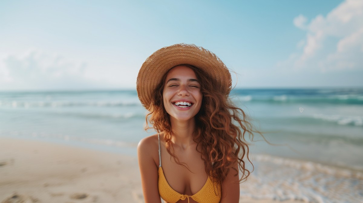 Frau am Strand mit Hut, die lächelt.