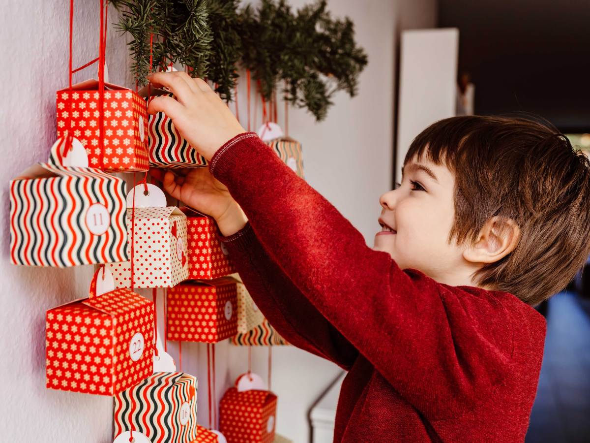 Kleiner Junge schaut vorsichtig in ein Kalendertürchen seines Adventskalenders.