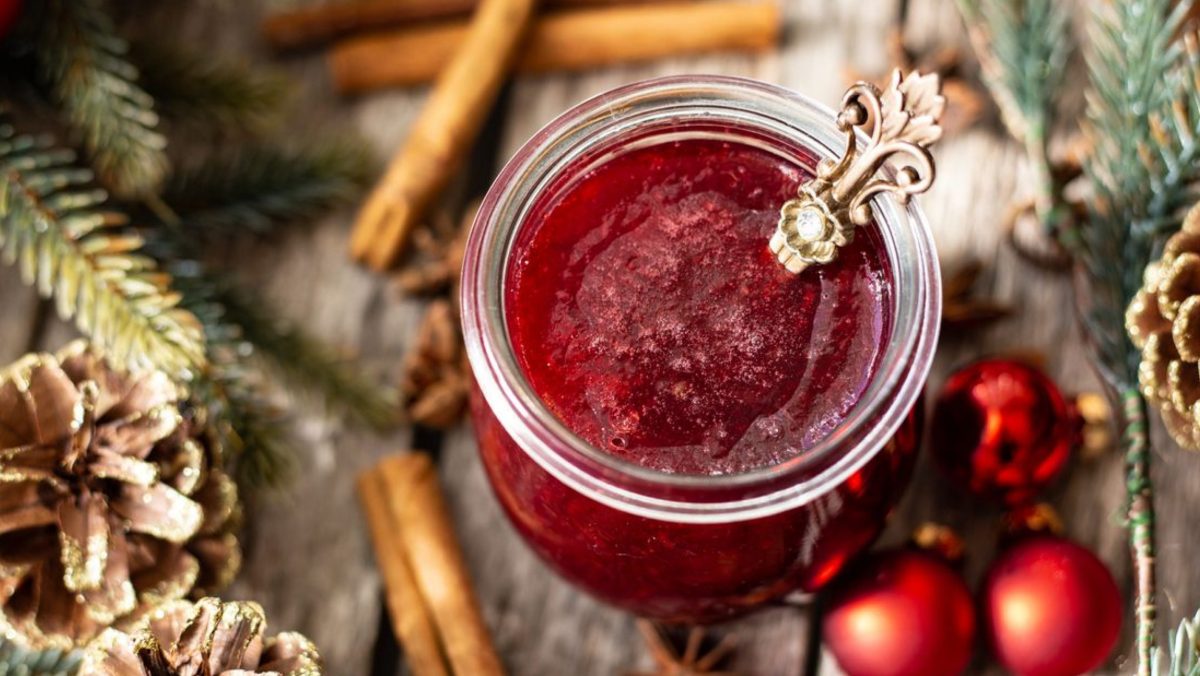 Rotes Fruchtgelee auf Holztisch mit Tannenzapfen daneben.