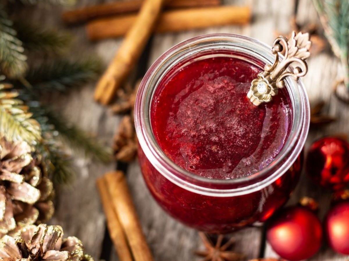 Rotes Fruchtgelee auf Holztisch mit Tannenzapfen daneben.