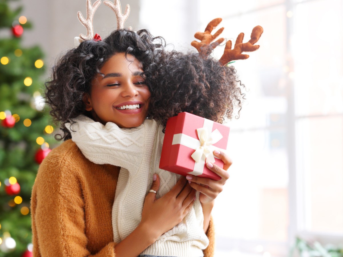 Mutter und Kind umarmen sich vor einem Weihnachtsbaum und übergeben ein Geschenk.