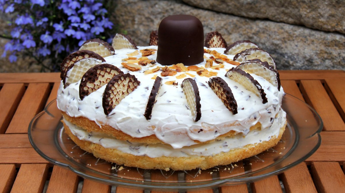 Torte mit Creme und Schokoküssen auf einem Kuchenteller.