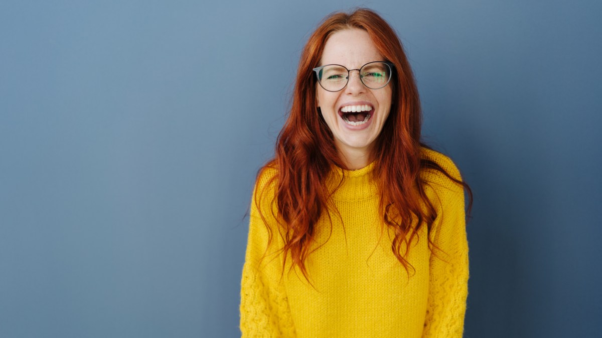 Lachende Frau mit roten Haaren und gelbem Pullover