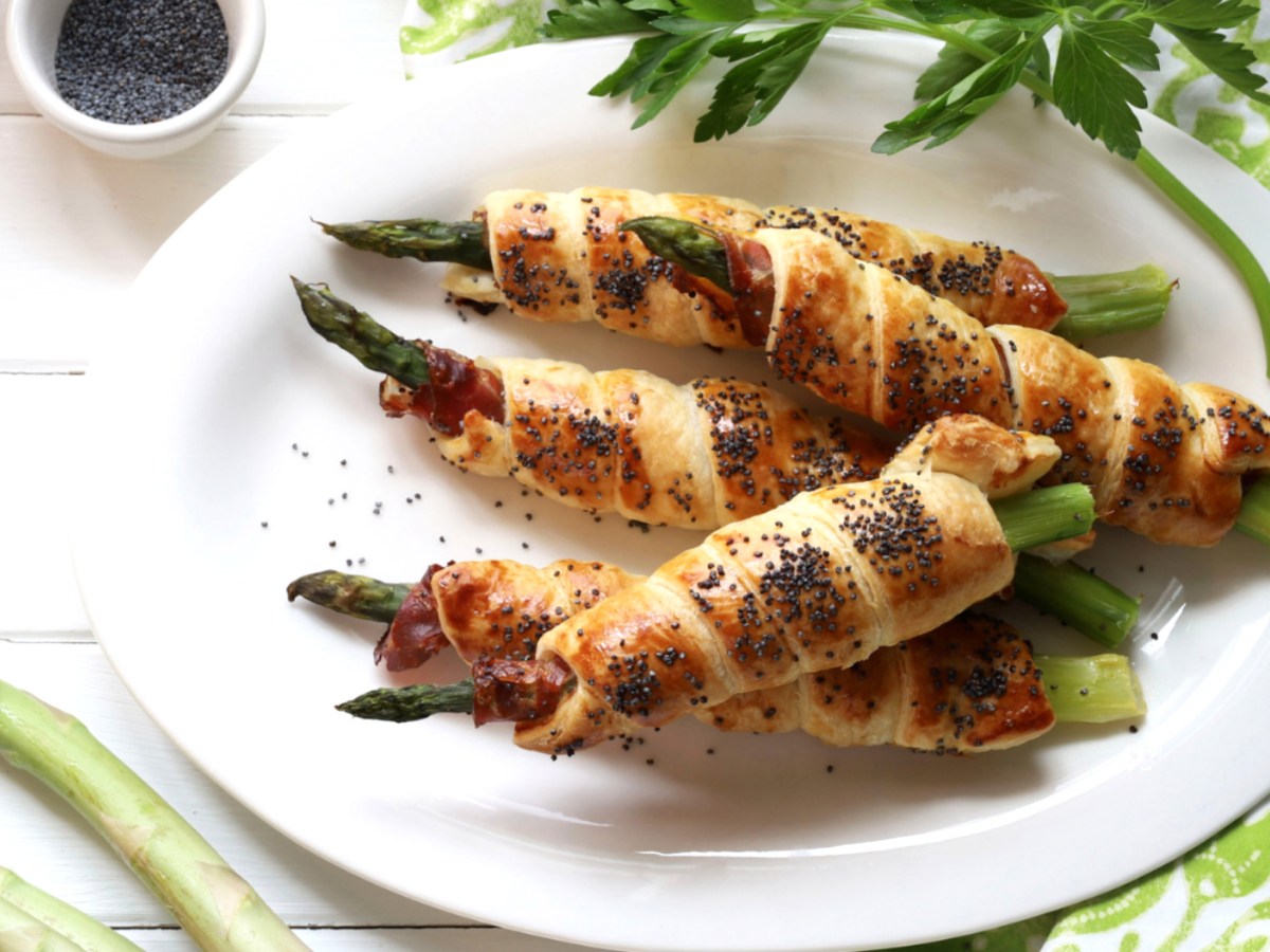 Grüner Spargel, der in Blätterteig umwickelt wurde, auf weißem Teller.