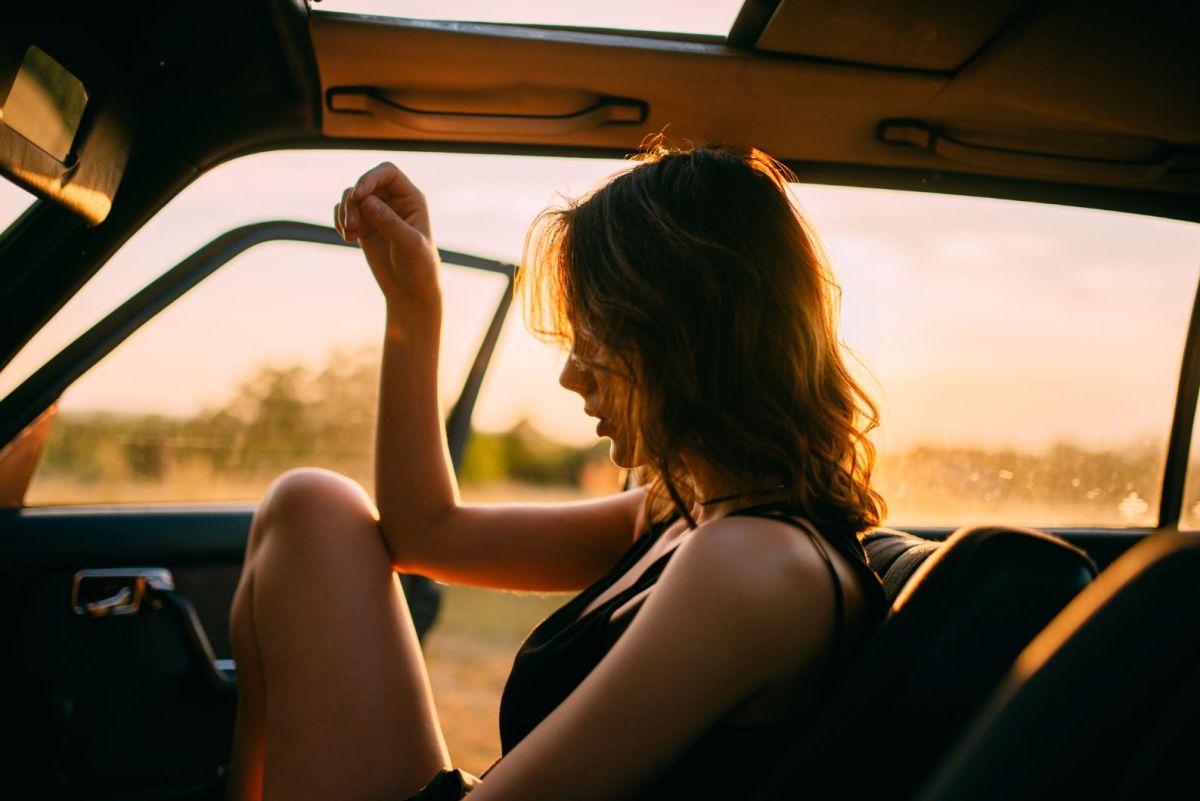 Junge Frau mit dunklen Haaren sitzt bei Sonnenuntergang im Auto bei offener Tür.