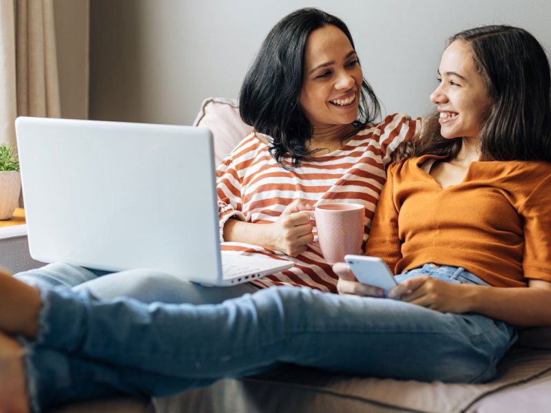 Mutter und Tochter sitzen vertraut und einander zugewandt auf der Couch.