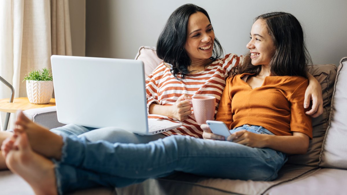 Mutter und Tochter sitzen vertraut und einander zugewandt auf der Couch.