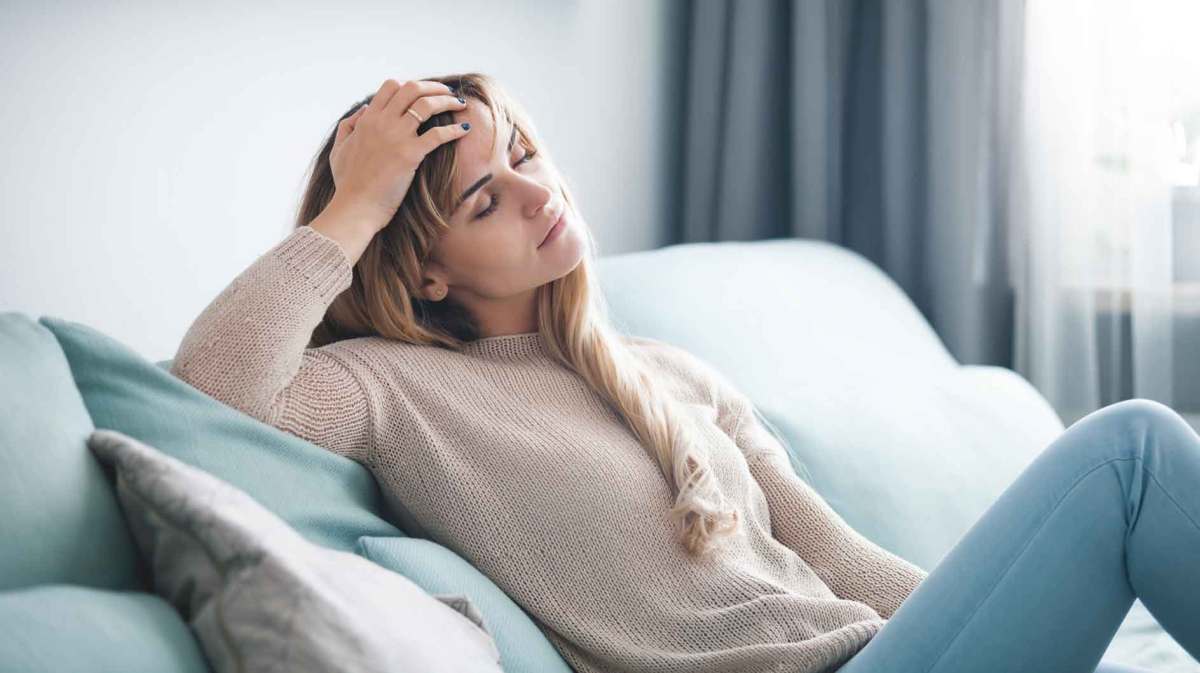 Frau liegt erschöpft auf der Couch und kann nicht mehr arbeiten.