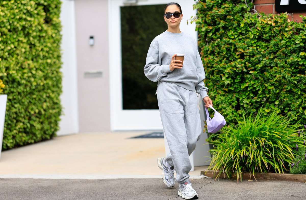 Frau mit grauen Outfit aus Sweater und Jogginghose und Sneaker vor Hecke