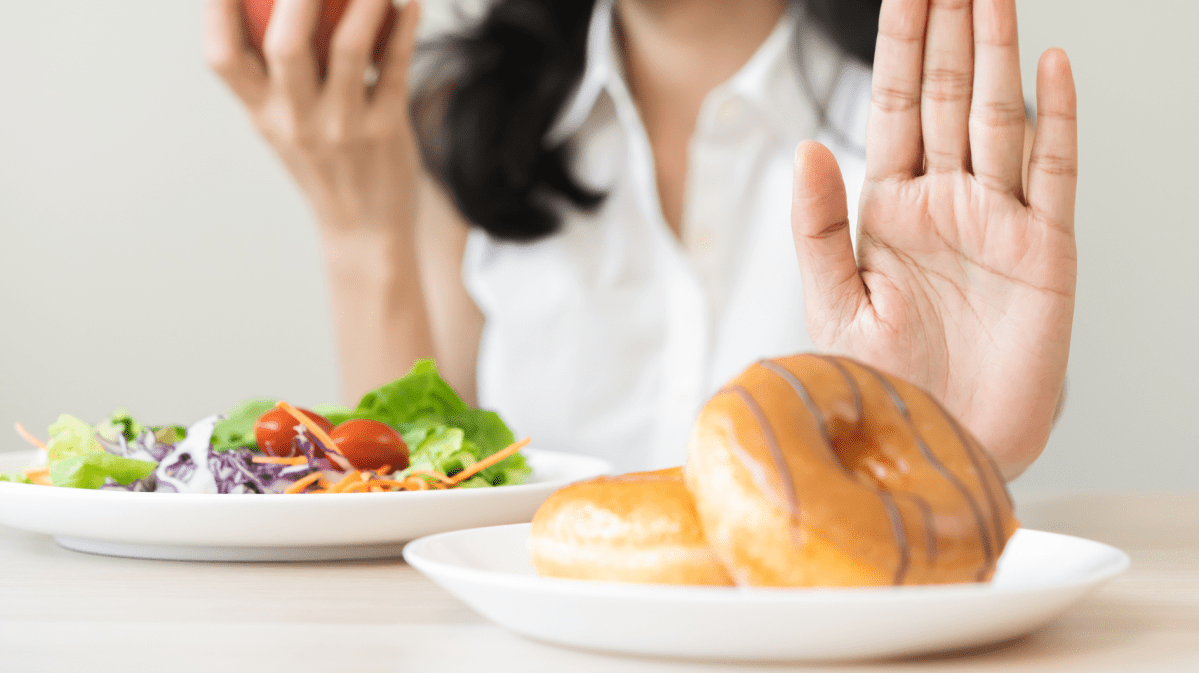 Frauenhand, die einen Salatteller vor sich hat und einen Teller voller Donuts zur Seite schiebt