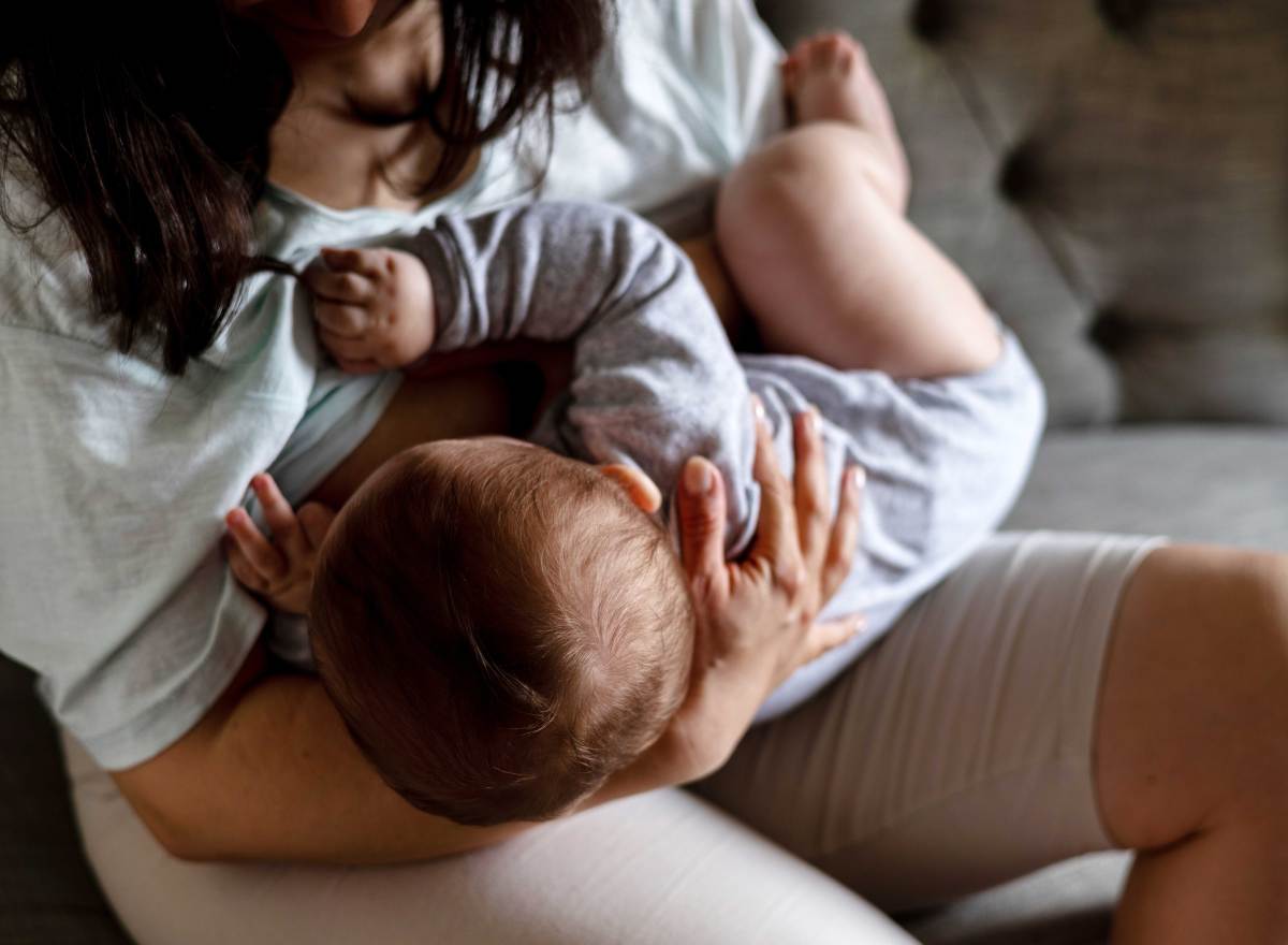 Mutter sitzt auf dem Sofa und stillt ihr ca. 6 Monate altes Kind.