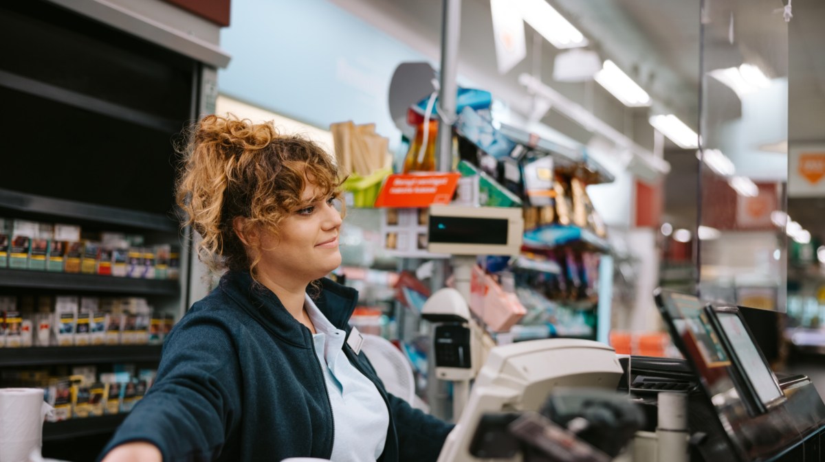 Frau an einer Supermarktkasse, die nett zur Seite lächelt