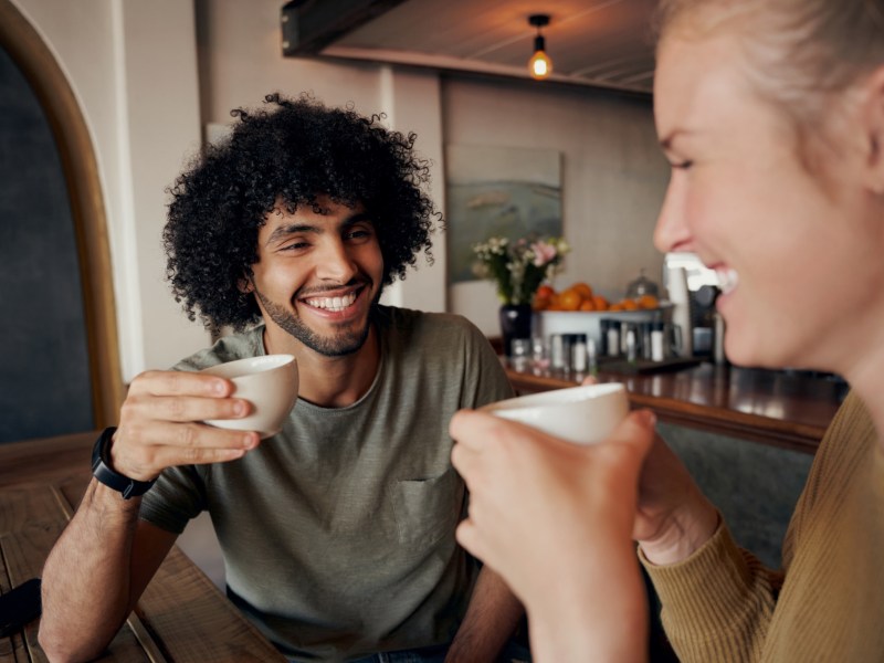 Mann und Frau beim Kaffeetrinken, die sich gegenseitig anlächeln