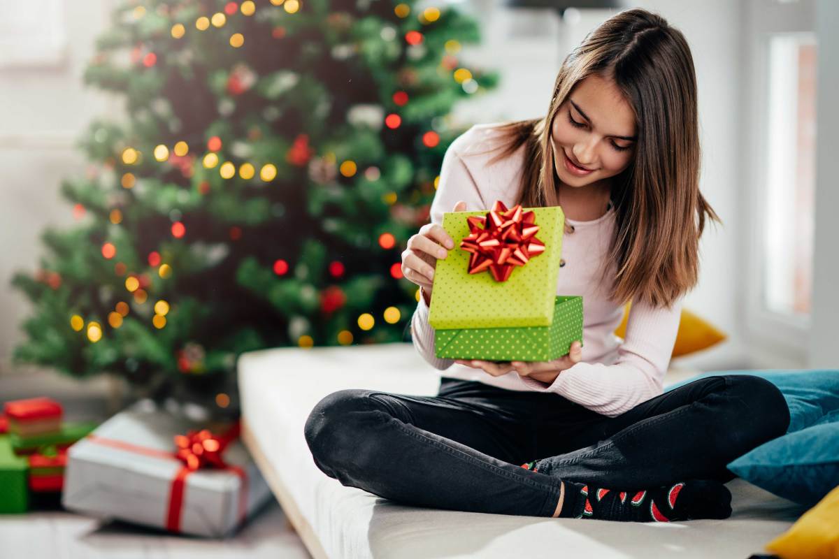 Teenager-Mädchen schaut neugierig in ein Weihnachtsgeschenk.