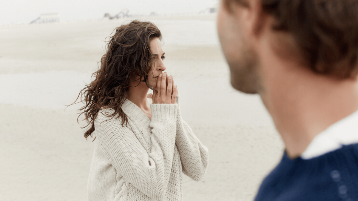 Frau steht am Strand und schaut nachdenklich in Ferne.