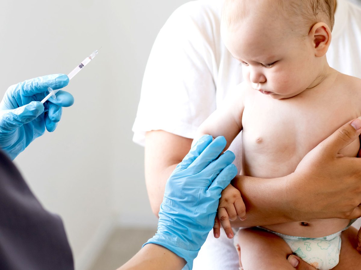 Kleines Baby hat gerade eine Impfung bekommen und schaut skeptisch zur Einstichstelle. Es wird von seinem Vater gehalten.