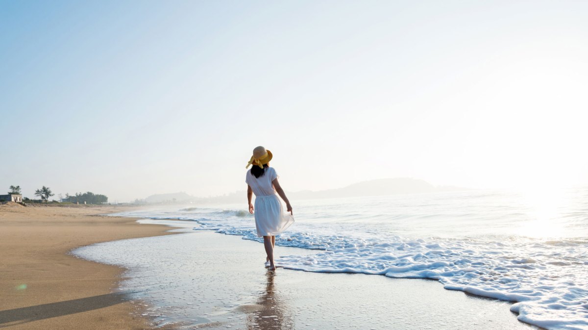 Frau im Sommerkleid mit Sonnenhut am Strand