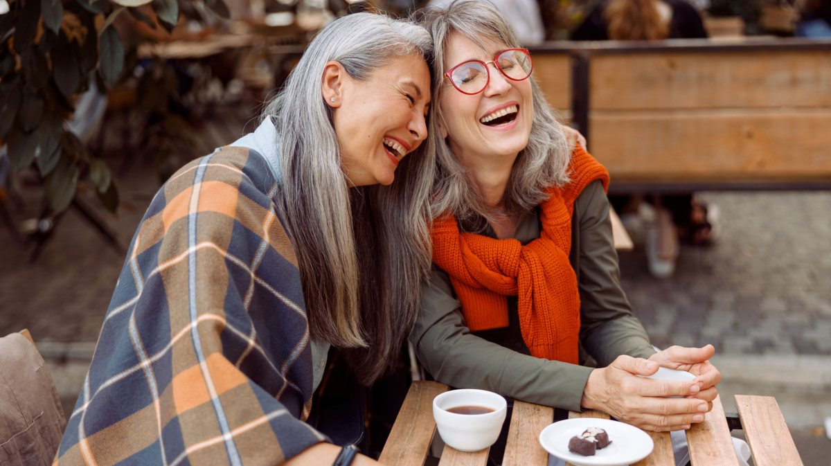 Zwei ältere Frauen sitzen in Café und lachen gemeinsam.